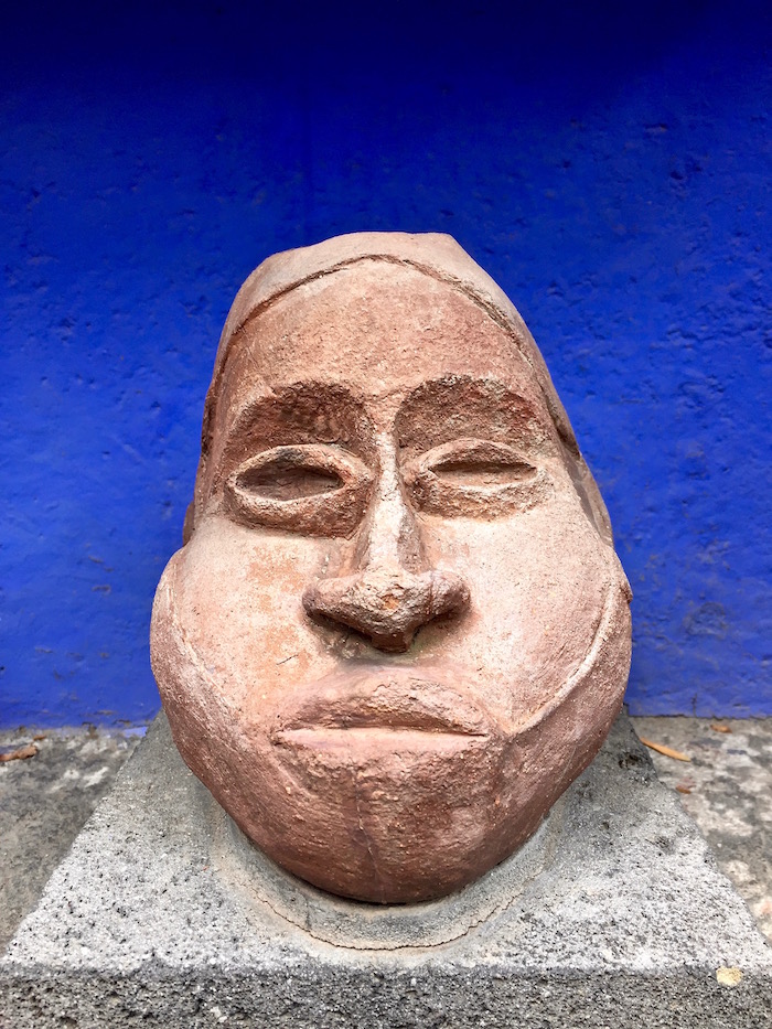 Big stone head in front of a blue wall inside Frida Kahlo's house