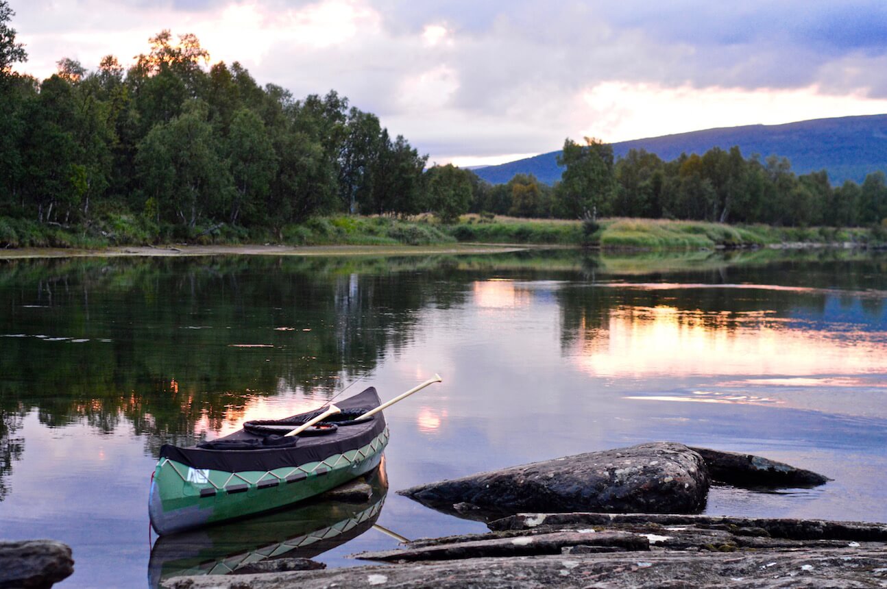 Our green Ally canoe at the river shore at sunset with the forest and the mountains in the back